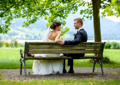 Brautpaar sitzt auf Bank am Schliersee, Hochzeitsportrait in idyllischem Park, fotografiert von Hochzeitsfotograf.