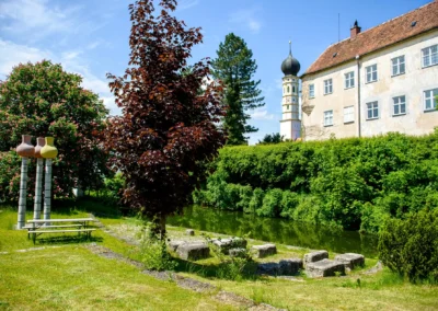 Hochzeit auf Gut Schloss Sulzemoos mit Garten, Baeumen, Sitzgelegenheiten und Turm im Hintergrund.