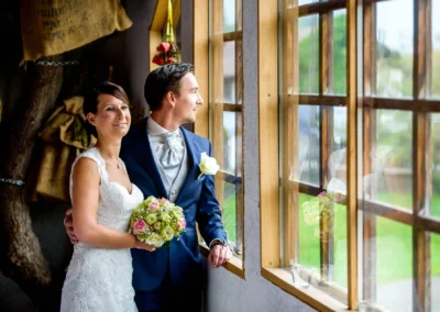 Brautpaar beim Fotoshooting in Moosach bei Grafing, die aus dem Fenster blicken, Hochzeitsfotografie in edlem Stil.