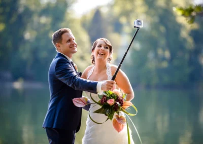 Brautpaar lacht beim Selfie mit Selfiestick am Wesslinger See, aufgenommen von Hochzeitsfotograf in Oberbayern.