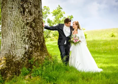 Brautpaar beim Hochzeitsfoto in Oberbayern, nahe München, posierend vor einem Baum auf einer Wiese.