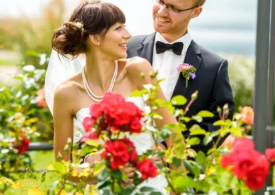 Brautpaarportrait am Schliersee, umgeben von roten Rosenbüschen, aufgenommen von einem Hochzeitsfotografen.