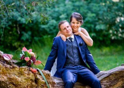 Brautpaarshooting am Wesslinger See, Hochzeitspaar auf Baumstamm, Blumenstrauß im Vordergrund, Hochzeitsfotografie.