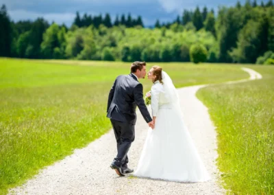 Brautpaar auf einem Weg, Hand in Hand beim Kuss. Hochzeitsfotografie nahe Holzkirchen in malerischer Umgebung.