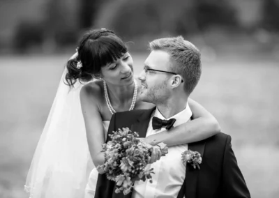 Brautpaar-portrait am Schliersee: Die Braut legt den Arm um den Bräutigam, beide lächelnd. Hochzeit, Oberbayern.