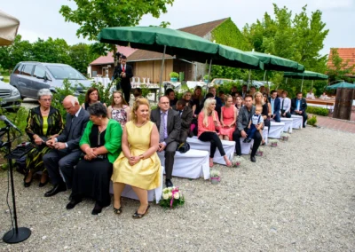 Gaste warten bei freier Trauung auf Hochzeit bei Schloss Sulzemoos, festlich gekleidet unter grunen Schirmen.