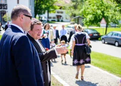 Hochzeitsreportage in Frauenkirche Osterwarngau, Gaeste im Gespraech nach kirchlicher Trauung bei sonnigem Wetter.