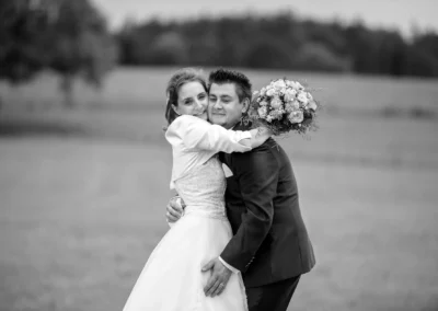 Brautpaar umarmt sich mit Blumenstrauss bei Hochzeitsfotografie in Holzkirchen, nahe Munchen. Schwarz-Weiss-Aufnahme.