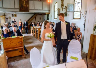 Brautpaar bei kirchlicher Trauung auf Gut Georgenberg, fröhliche Gäste in der Kirche, Hochzeitsfoto in Oberbayern.