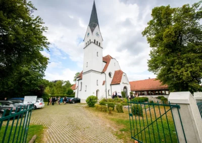 Hochzeitsfoto bei kirchlicher Trauung in neuapostolischer Kirche Miesbach, sonniger Tag, Gaeste versammeln sich.