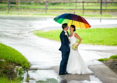 Brautpaarshooting im Regen mit buntem Schirm in Moosach bei Grafing. Hochzeitsfotograf fängt den Moment ein.