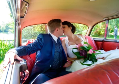 Brautpaarshooting im Auto am Wesslinger See, Braut in weissem Kleid, Bräutigam in blauem Anzug für Hochzeitsfoto.