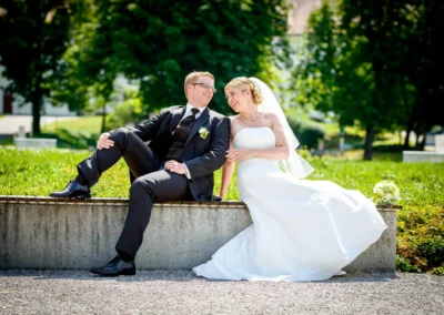 Hochzeitspaar sitzt entspannt auf einer Mauer im Freien, Hochzeitsfotografie nahe Kloster Fuerstenfeld.