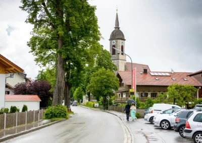 Paar mit Regenschirm neben Kirche Mariä Heimsuchung, Holzkirchen. Hochzeit in Oberbayern fotografiert.