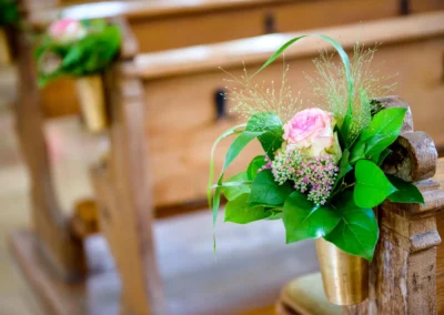 Blumenschmuck an Kirchenbank bei Hochzeitsreportage in St. Vitus nahe Gilching, festliche Dekoration auf kirchlicher Trauung.