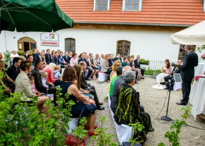 Freie Trauung bei einer Hochzeit im Gut Schloss Sulzemoos mit sitzenden Gaesten und Brautpaar.