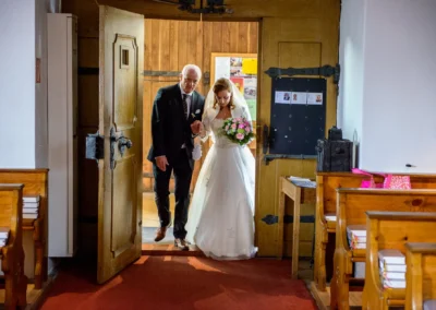Braut schreitet mit Begleiter in Kirche fuer Hochzeitsreportage in Grosshartpenning. Hochzeitsfotograf dokumentiert.