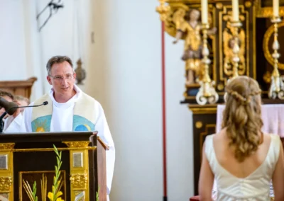 Priester bei kirchlicher Trauung in St. Benedikt Gelting, Braut im Vordergrund, Hochzeitsfotografie.