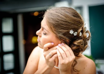 Junge Frau mit Blumen im Haar steckt Ohrring an; sanftes Licht, Hintergrund unscharf.