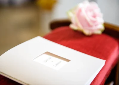 Hochzeitsfoto in Ottendichl bei kirchlicher Trauung. Programmheft und rosa Rose auf rotem Stuhl.