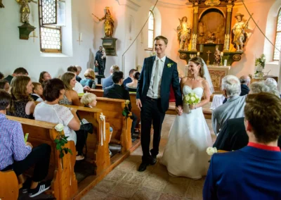 Brautpaar beim Auszug nach kirchlicher Trauung, Hochzeit auf Gut Georgenberg, Gäste sitzen in der Kirche.