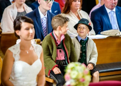Zwei lachende Kinder in Tracht bei einer kirchlichen Trauung in der Dorfkirche Moosach, Hochzeitsfotografie Bayern.