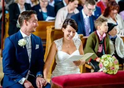 Brautpaar während der kirchlichen Trauung in der Dorfkirche Moosach, Bayern, umgeben von Gästen. Hochzeitsreportage.