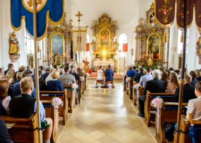 Hochzeitsfotografie in der Dorfkirche Moosach: Brautpaar bei der kirchlichen Trauung, umgeben von Gaesten.