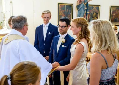 Brautpaar bei kirchlicher Trauung in St. Benedikt Gelting, Hochzeitsfoto zeigt emotionalen Moment mit Priester.