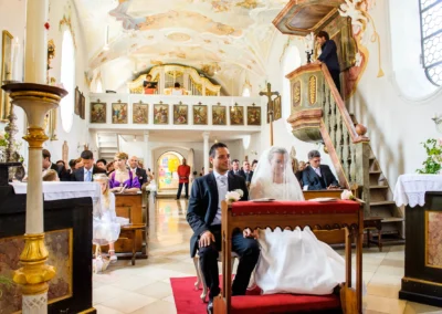 Kirchliche Trauung in Ottendichl bei Muenchen, Brautpaar vor rotem Teppich in festlicher Kirche sitzend.