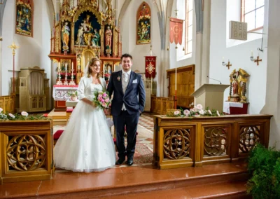 Brautpaar in der Kirche Mariae Heimsuchung, Holzkirchen. Hochzeitsfoto mit Altar im Hintergrund, festlicher Moment.