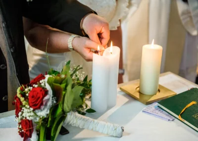 Brautpaar entzündet Kerzen bei kirchlicher Hochzeit in der Frauenkirche Osterwarngau, begleitet von einem Blumenstrauß.