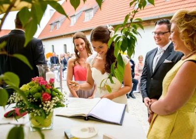 Braut unterzeichnet Freie Trauung auf Gut Schloss Sulzemoos, umgeben von Freunden, bei sonniger Hochzeitszeremonie.
