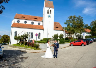 Brautpaar vor Kirche St. Vitus bei Hochzeit in Gilching, Hochzeitsfoto zeigt romantischen Moment nach Trauung.
