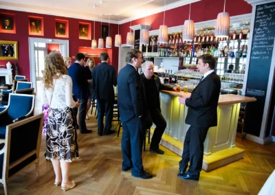 Gäste bei Hochzeitsfeier im Kurhaus Bad Tölz, elegant gekleidet, stehen an der Bar und unterhalten sich.