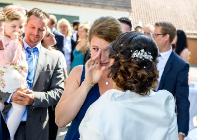 Eine emotionale Szene bei einer Hochzeit nahe München, eine Frau wischt sich eine Träne ab, während sie die Braut umarmt.