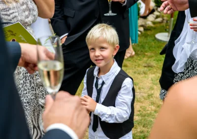 Ein Junge bei einer Hochzeit in Gut Georgenberg, umgeben von elegant gekleideten Gaesten mit Champagner.