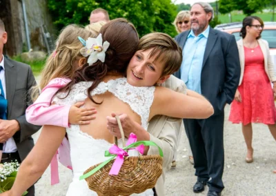 Braut umarmt Kind bei freier Trauung auf Gut Schloss Sulzemoos, umgeben von Gratulanten. Hochzeitsfoto-Moment.