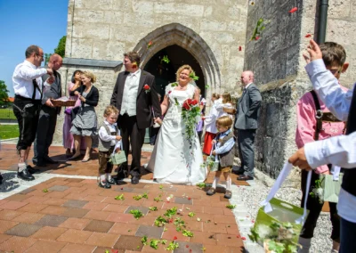 Brautpaar verlasst Kirche in Warngau, umgeben von Hochzeitsgaesten. Hochzeitsfotografie in Bayern.