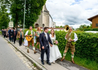 Hochzeitszug mit Brautpaar und Musikern in traditioneller Tracht in Oberbayern. Hochzeitsfotografie im Kreis Miesbach.