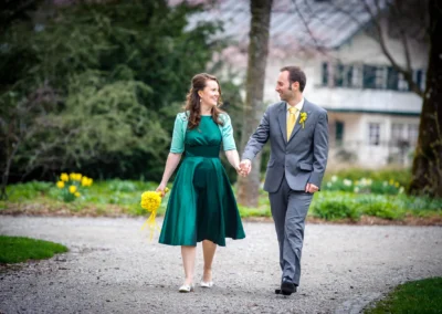 Brautpaar beim Hochzeitsportrait im Kurpark Bad Tölz. Das Paar spaziert Hand in Hand, umgeben von frischem Gruen.