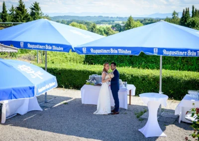 Brautpaar unter blauem Sonnenschirm bei der Hochzeitsfeier im Gasthof zur Post nahe Starnberger See.