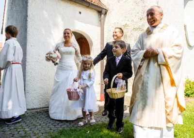 Brautpaar und Priester bei der kirchlichen Trauung in Ottendichl, Kinder mit Koerbchen. Hochzeitsfotografie Oberbayern.