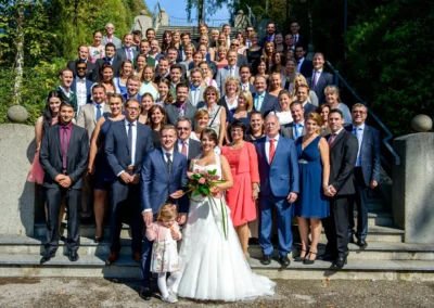 Gruppenfoto bei einer Hochzeit nahe München, viele Gäste auf Treppe versammelt, Brautpaar vorne, Hochzeitsfoto.