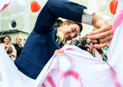 Bräutigam schneidet Herz in Tuch, Hochzeitsgesellschaft schaut zu. Hochzeitsfotografie in Oberbayern.