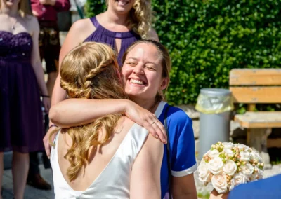 Zwei Frauen umarmen sich herzlich bei einer Hochzeit, nahe dem Starnberger See, eine haelt einen Blumenstrauss.