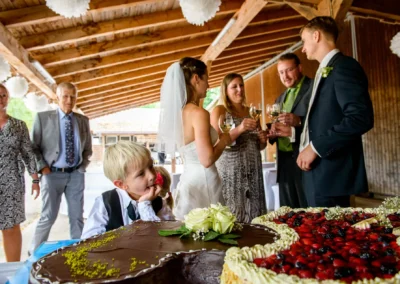 Hochzeitsreportage auf Gut Georgenberg mit Brautleuten und Gaesten beim Anstoßen, Hochzeitstorte im Vordergrund.