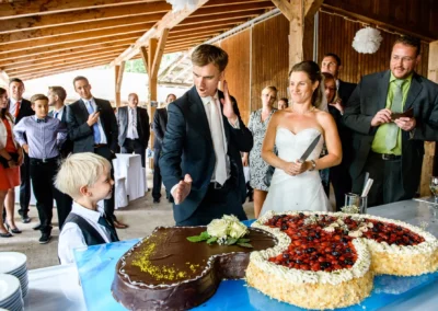 Brautpaar beim Anschneiden der Hochzeitstorte auf Gut Georgenberg, umgeben von Gästen, Hochzeitsreportage.