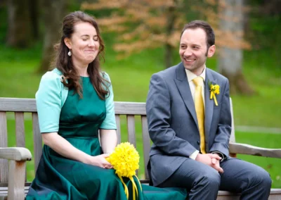 Brautpaar auf einer Bank im Kurpark Bad Toelz. Hochzeit mit gelbem Blumenstrauss und gruenem Kleid. Hochzeitsfoto.