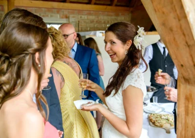 Braut bei der Hochzeit auf Gut Schloss Sulzemoos, lacht mit Gaesten bei Sektempfang. Hochzeitsfoto zeigt froehliche Stimmung.
